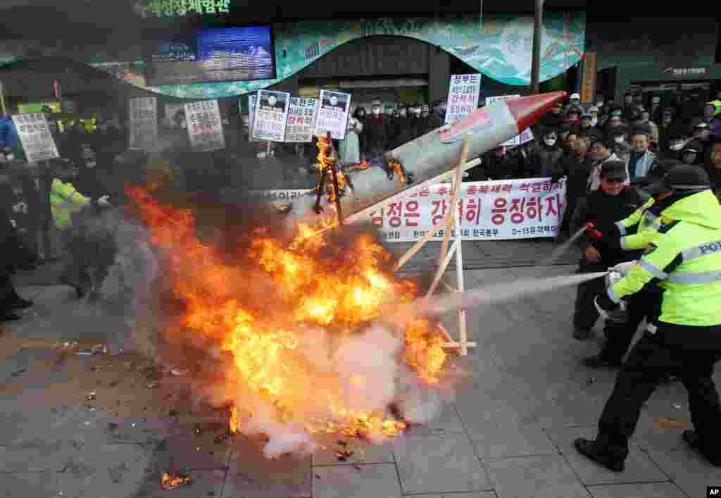 2012年12月12日，韩国抗议者在首尔举行的谴责朝鲜发射火箭的集会上焚烧模拟火箭，警察赶紧动用灭火器。