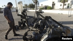 Seorang personil militer LIbya memeriksa mobil yang meledak dekat Akademi Polisi Wanita setempat, di Tripoli, Minggu (19/8). women's police academy, a Li