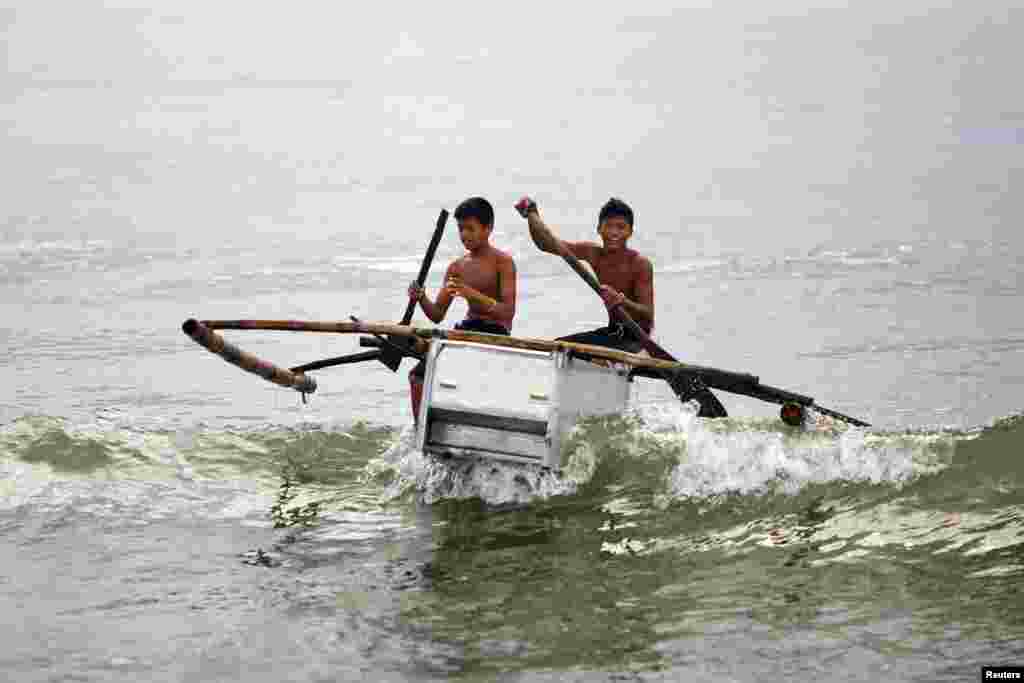 Dua anak laki-laki mengendalikan perahu mereka yang terbuat dari kulkas yang rusak dan bambu di pantai Tanauan, Filipina. Banyak nelayan setempat memanfaatkan kulkas yang rusak sebagai perahu darurat pasca bencana topan Haiyan.