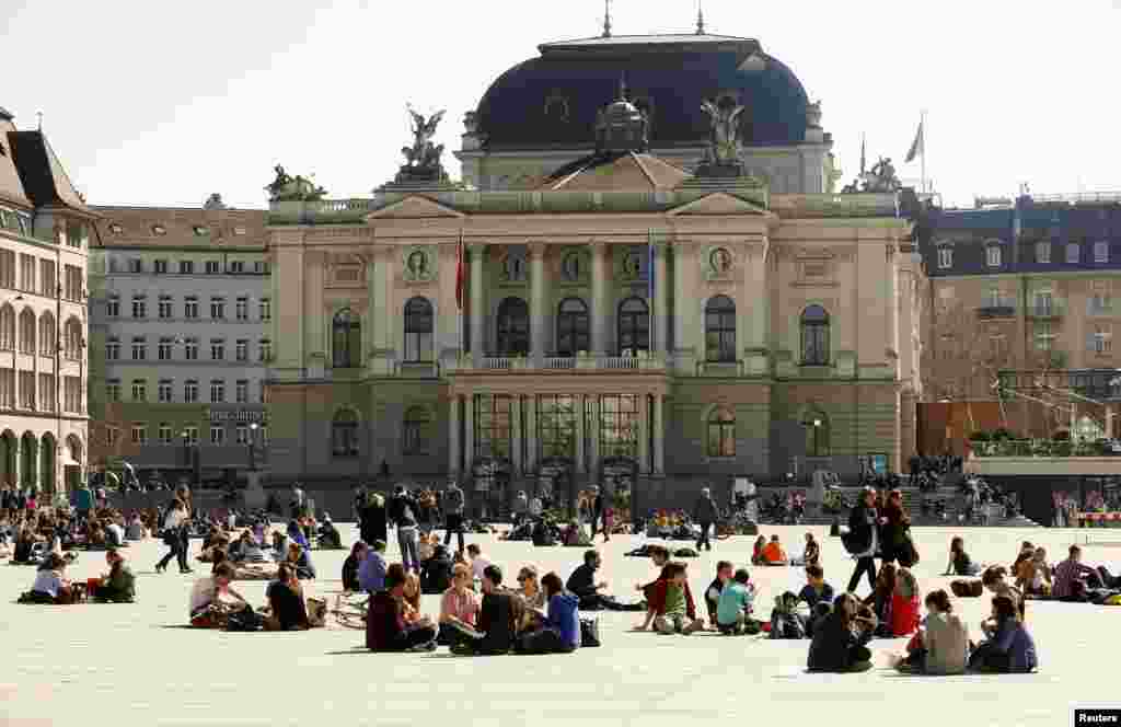 Warga Swiss menikmati cuaca hangat di Lapangan Sechselaeutenplatz di depan gedung opera di kota Zurich. 
