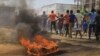 Protesters walk past a burning tyre in the Eastern Congolese town of Beni, Friday Dec. 28, 2018, as they demonstrate against the election postponed until March 2019, announced by Congo's electoral commission for Beni residents that is blamed on a deadly Ebola outbreak. 