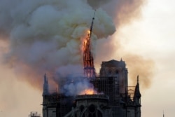 FILE - The steeple and spire of the landmark Notre-Dame Cathedral collapses as the cathedral is engulfed in flames in central Paris on April 15, 2019.