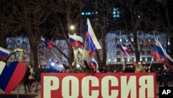 Orang-orang mengibarkan bendera nasional Rusia untuk merayakan, di pusat Donetsk, wilayah yang dikuasai oleh militan pro-Rusia, Ukraina timur, Senin malam, 21 Februari 2022. (Foto: AP)