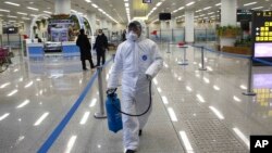 Un homme en tenue de protection transporte du désinfectant à l'aéroport de Pyongyang en Corée du Nord, le 1er février 2020.