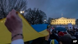 Sejumlah orang memegang bendera Ukraina dalam ukuran besar dalam aksi protes Invasi Rusia terhadap Ukraina yang berlangsung di depan Gedung Putih, Washington, pada 24 Februari 2022. (Foto: AP/Andrew Harnik)