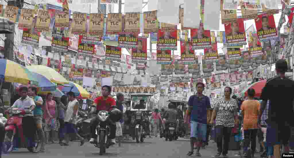Election posters for the midterm elections hang along a street as residents walk to a polling precinct in Taguig, Metro Manila, May 13, 2013.