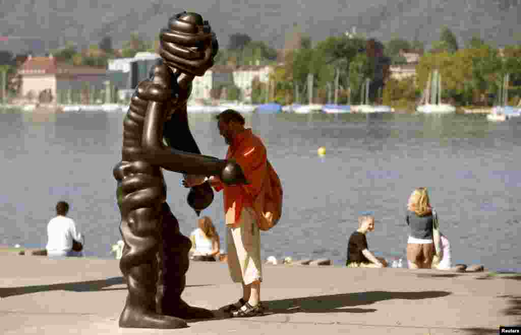 Seorang pria berdiri di samping patung 'Vier Grosse Geister' (Empat Hantu Besar) karya seniman Jerman Thomas Schuette di tepi Danau Zurich, Swiss.