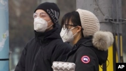 Residents wearing masks wait at a traffic light in Beijing, China Thursday, Feb. 13, 2020.