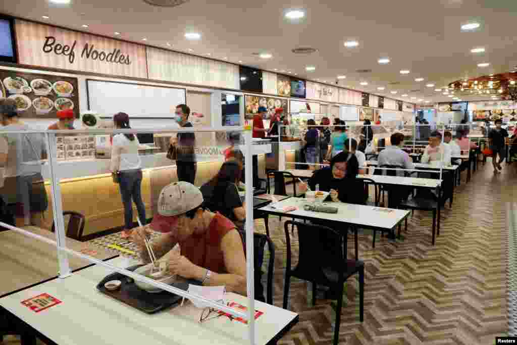 Clientes comen en una mesa instalada con divisores de plexiglás en un patio de comidas en Singapur cuando la ciudad estado reabre su economía en medio del brote de la enfermedad del coronavirus (COVID-19).