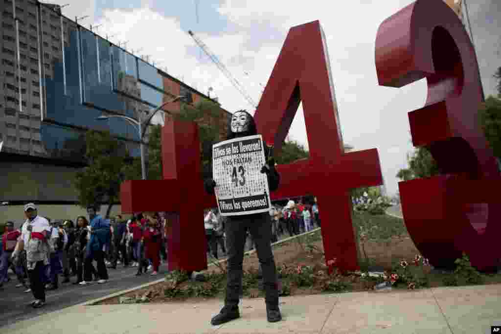 A masked protestor poses with a sign reading "We are missing 43. They took them alive. We want them back alive" in front of a recently erected monument to the missing rural teachers college students from Guerrero state, during a May Day march in Mexico City, May 1, 2015.
