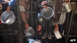 Warga Palestina berkumpul untuk menerima makanan yang dibagikan di sepanjang pinggir jalan di kamp pengungsi Nuseirat di Jalur Gaza, 11 Januari 2025, ketika mediator AS, Qatar, dan Mesir berupaya mencapai kesepakatan penyanderaan dan gencatan senjata.(Foto: Eyad Baba via AFP)