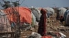 FILE - A Somali woman carries wood to make a shelter in an internally displaced people (IDP) camp, Dec. 18, 2018.