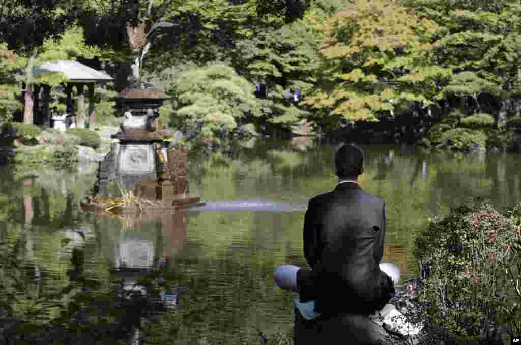 Seorang pria duduk di atas batu dan melakukan meditasi di taman Hibiya di Tokyo, Jepang.