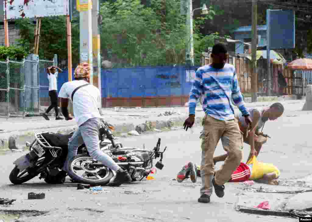 People help a motorcycle rider after he had an accident while trying to avoid being hit by stray bullets during clashes between gangs and security forces, in Port-au-Prince, Haiti, Nov. 11, 2024.