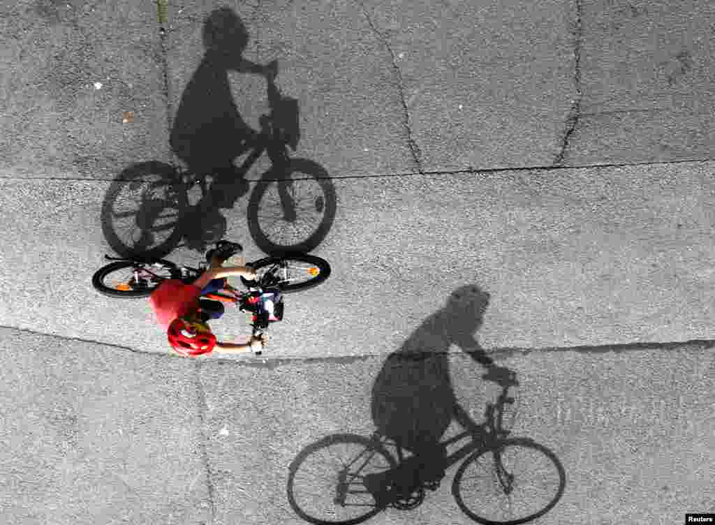 A woman and a child cast shadows as they ride their bicycles on a sunny day in Vienna, Austria.