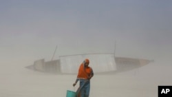 Seorang perempuan India membawa satu ember berisi air minum ketika berjalan di lumpur kering di tengah tiupan pasir, sepanjang sungai Brahmaputra di malam Hari Air Sedunia di Gauhati, India, 21 Maret 2014. (Foto: dok.)