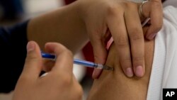 FILE - A woman gets a vaccination from a nurse in Mexico City, Jan. 27, 2014.