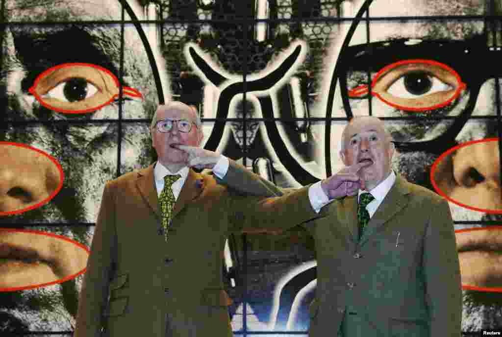 Italian artist Gilbert Proesch (R) and British artist George Passmore, known as Gilbert & George, pose with their artwork "Scapegoating" during the launch of their new exhibition "Scapegoating" at the White Cube gallery in Bermondsey, London.