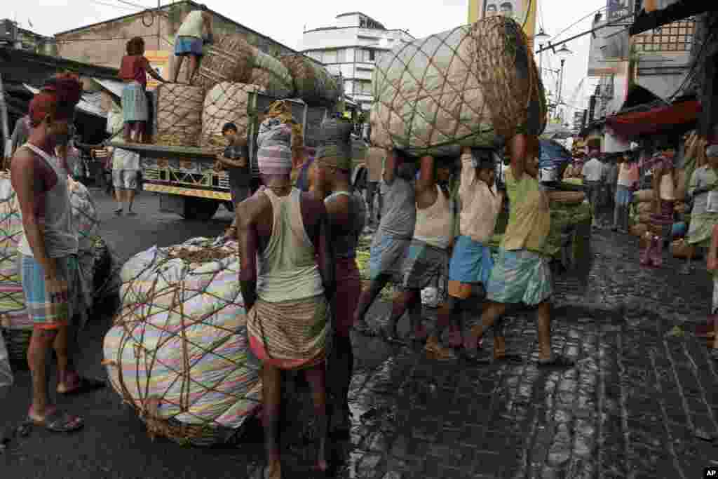 Para buruh India membawa keranjang raksasa berisi buah-buahan ke pasar grosir di Kolkata.