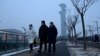 People walk along a path as the Beijing Olympic Tower is seen during a smoggy day in Beijing, Jan. 24, 2022. 
