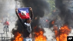 Seorang demonstran mengibarkan bendera Haiti dalam aksi protes meminta peungunduran diri Perdana Menteri Ariel Henry di Port-au-Prince, pada 1 Maret 2024. (Foto: AP/Odelyn Joseph)