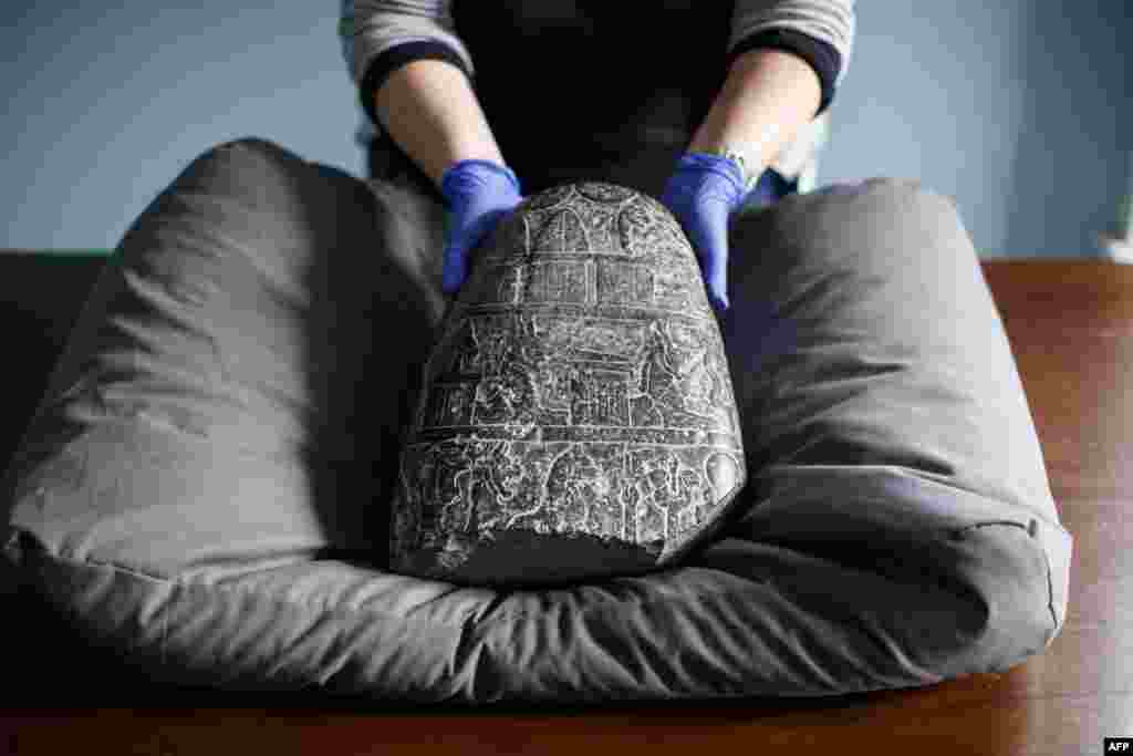A gallery assistant poses with a Babylonian cuneiform kudurru (boundary stone) which was looted from Iraq at the British museum in London. The kudurru, seized at London's Heathrow airport in 2012, was handed over to representatives of the Iraq embassy at the British museum.