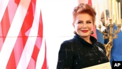 FILE - Georgette Mosbacher stands next to an American flag after receiving her credentials as United States ambassador to Poland in Warsaw, Sept. 6, 2018. 