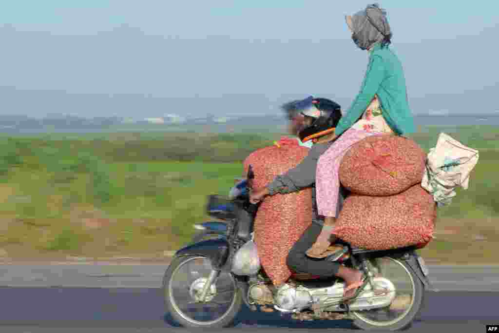 Seorang pria membawa tiga karung kacang dengan motornya, sementara seorang perempuan membonceng di atas karung di Phnom Penh, Kamboja.