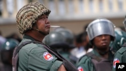 Cambodian riot police officers stand guard at a blockade in a main street as teachers stage a protest march in Phnom Penh, Cambodia, Sunday, Oct. 5, 2014.