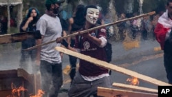 A demonstrator wearing a mask throws a plank of wood into a flaming barricade during a protests in Santiago, Chile, Saturday, Oct. 19, 2019. The protests started on Friday afternoon when high school students flooded subway stations, jumping…