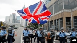 FILE - A woman waves a British flag as policemen in anti-riot gear stand guard against protesters on a closed-off road near the Legislative Council in Hong Kong, June 12, 2019.