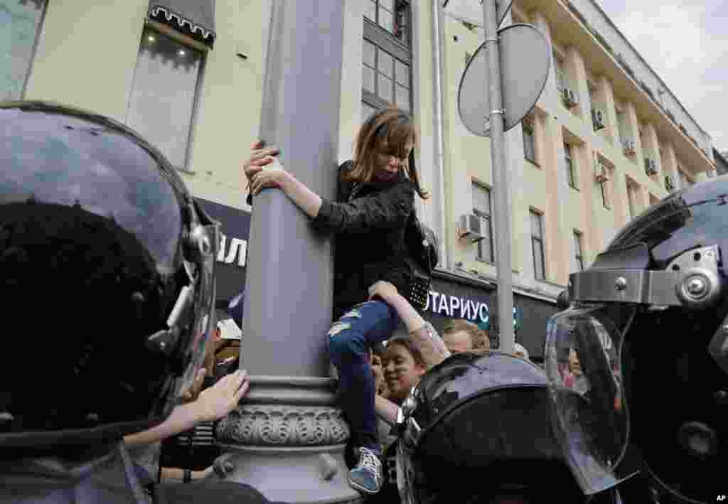 Seorang demonstran ditarik turun dari tiang listrik oleh oleh rekan-rekannya saat aksi protes oposisi di kota Moskow, Rusia.