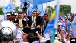 Sam Rainsy, center, president of Cambodia National Rescue Party (CNRP) greets his supporters together with his party's Vice President Kem Sokha, on Rainsy's left, on his arrival at Phnom Penh International Airport in Phnom Penh, Cambodia, Friday, July 19, 2013. Thousands of cheering supporters greeted Cambodian opposition leader Sam Rainsy as he returned from self-imposed exile Friday to spearhead his party's election campaign against well-entrenched Prime Minister Hun Sen. (AP Photo/Heng Sinith)