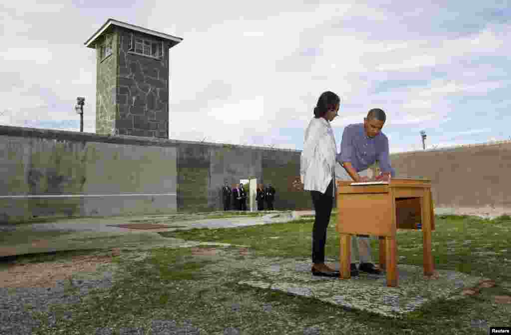 U.S. President Barack Obama writes in a guest book as he tours Robben Island with first lady Michelle Obama, near Cape Town, June 30, 2013.