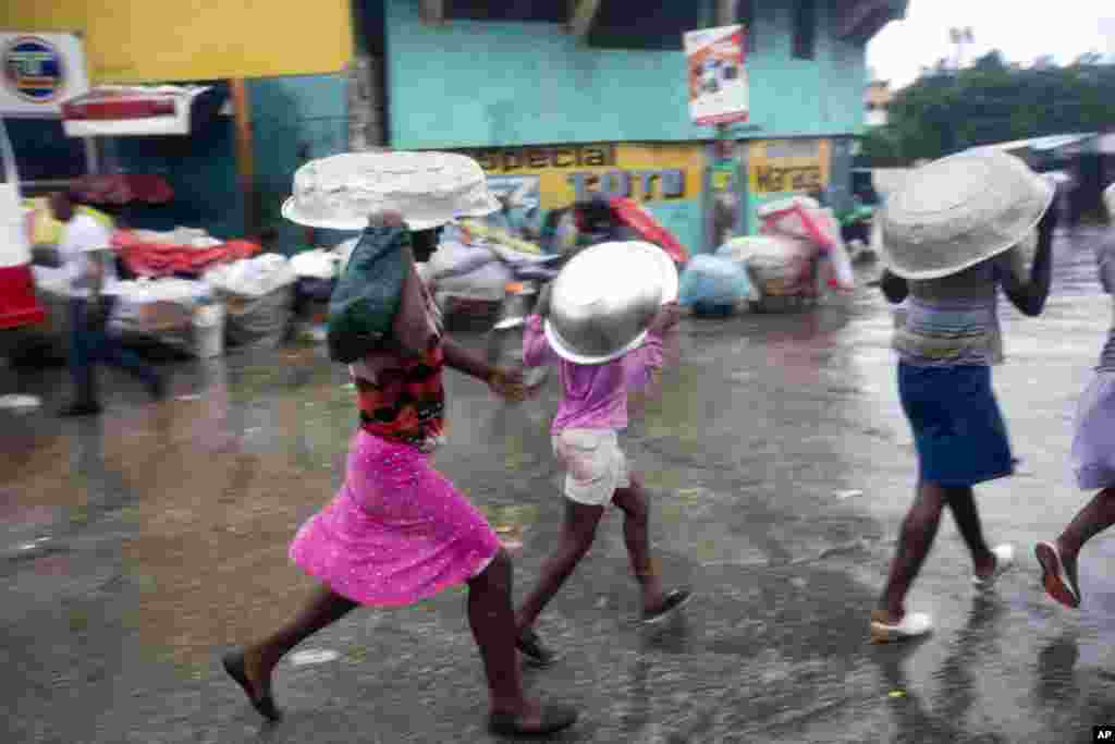 Warga menutupi kepalanya dengan panci saat berjalan di tengah hujan yang dibawa Badai Matthew di Port-au-Prince, Haiti (4/10). (AP/Dieu Nalio Chery)