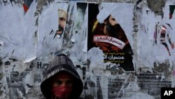 FILE - A Bahraini anti-government protester watches for riot police from in front of a wall with posters of a Shiite cleric executed in Saudi Arabia and other opposition posters that have been torn by authorities in Sitra.