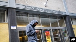 A pedestrian wears a face mask while standing outside the High School of Economics & Finance closed due to coronavirus concerns, Monday, March 16, 2020, in New York. 