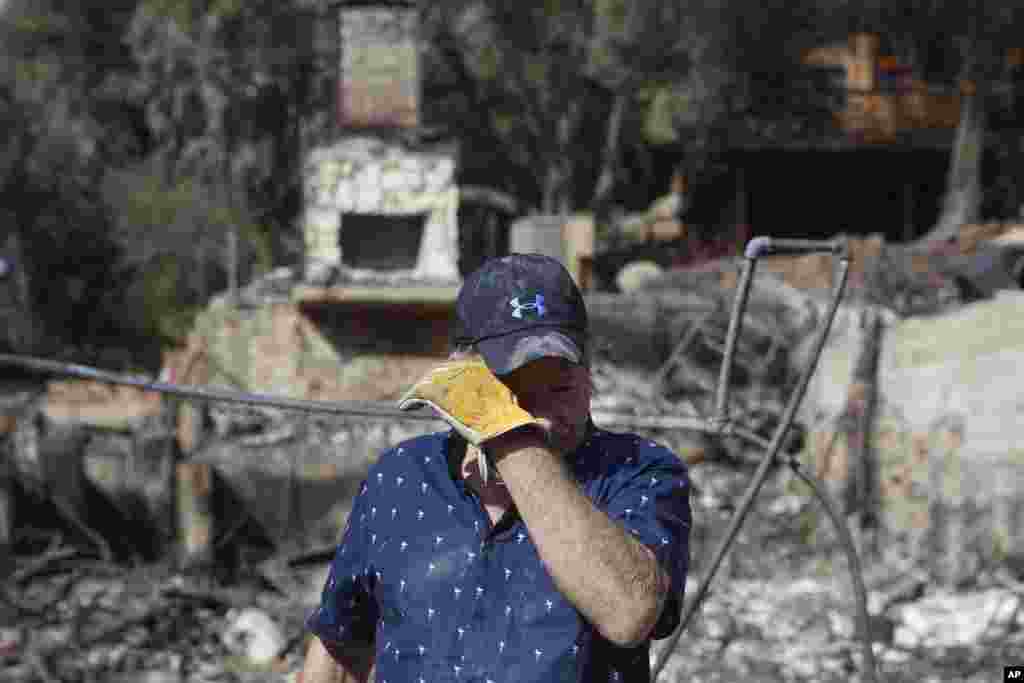 Roger Kelton, 67, wipes his tears while searching through the remains of his mother-in-law's home burned down by the Woolsey Fire, Nov. 13, 2018, in Agoura Hills, Calif.