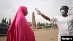 Mhudumu wa afya nchini Nigeria apima joto la mwanamke ili kubaini iwapo huenda anaugua.