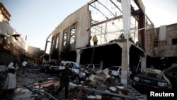 FILE - People stand at the site of an airstrike on a hall where a wake was being held in Sana'a, Yemen, Oct. 8, 2016.