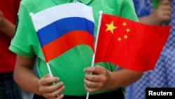 一名中国男孩在北京人大会堂外手持中俄两国国旗欢迎到访的俄罗斯总统普京。（2016年6月25日）