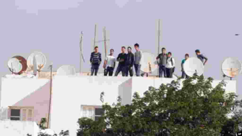 Des jeunes tunisiens, debout sur un toit, regardent les opérations policières en cours après une fusillade avec des militants dans la banlieue Oued Ellil de Tunis, Tunisie, le jeudi 23 octobre 2014. Un agent de sécurité a été tué dans lae fusillade. (AP Photo/Aimen Zine)