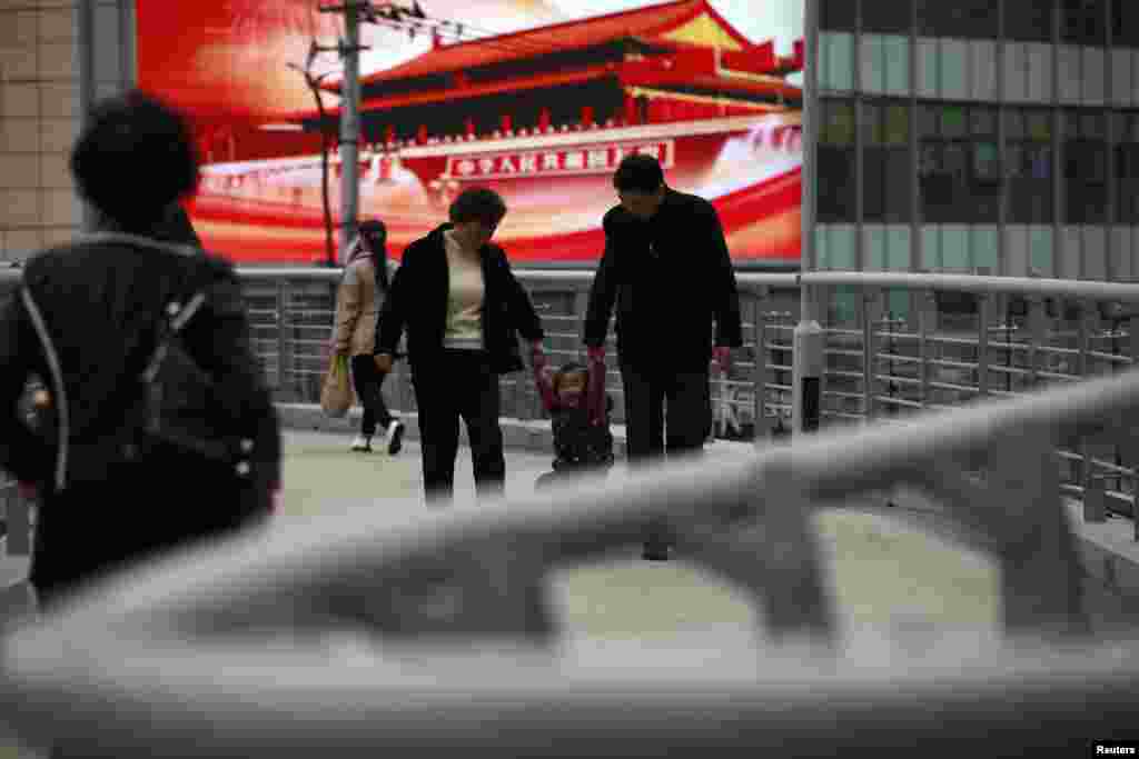 2012年11月8日，一户人家从上海一座天桥上树立的大型宣传屏幕前走过。