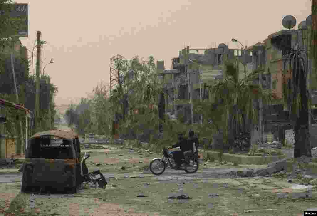 People ride a motorcycle past a damaged car in Deir al-Zor, Syria, April 4, 2013.