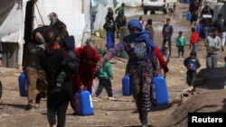 FILE - Syrian refugees walk as they carry containers at a tent settlement in Lebanon's Bekaa Valley, March 12, 2021.