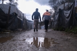 FILE - Migrants walk past makeshift tents outside the perimeter of the overcrowded Moria refugee camp on the northeastern Aegean island of Lesbos, Greece, March 11, 2020.