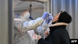 Un membre du personnel médical portant un équipement de protection prend un écouvillon d'un visiteur pour tester le coronavirus Covid-19 dans une station de test temporaire à l'extérieur d'une gare de Séoul le 16 décembre 2020 (Photo par Jung Yeon-je / AFP)