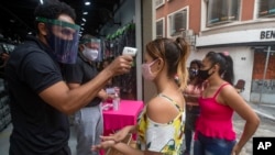 Seorang konsumen mengenakan masker sedang diperiksa suhu tubuhnya sebelum memasuki sebuah toko, di Sao Paulo, Brazil, 10 Juni 2020. 
