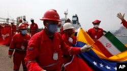Seorang pekerja Venezuela memegang bendera Iran dalam upacara penyambutan kedatangan tanker minyak Iran, Fortune, di Kilang El Palito, dekat Puerto Cabello, Venezuela, 25 Mei 2020.