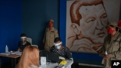 Miembros del Consejo Electoral venezolano, con tapabocas y escudos protectores, verifican la autenticidad de los datos de votantes en Caracas. 